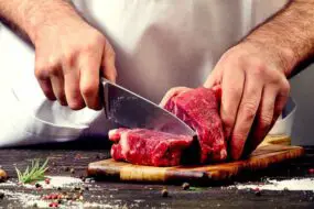A chef cutting raw beef with a knife
