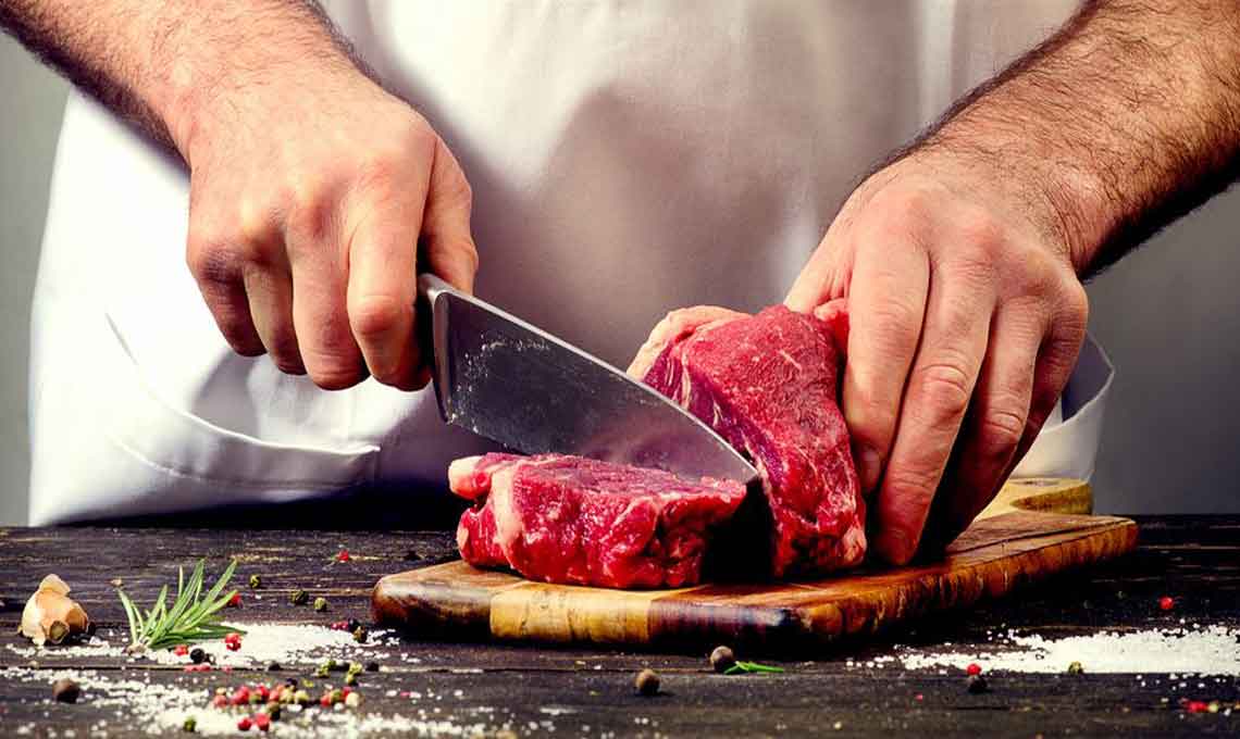 A chef cutting raw beef with a knife